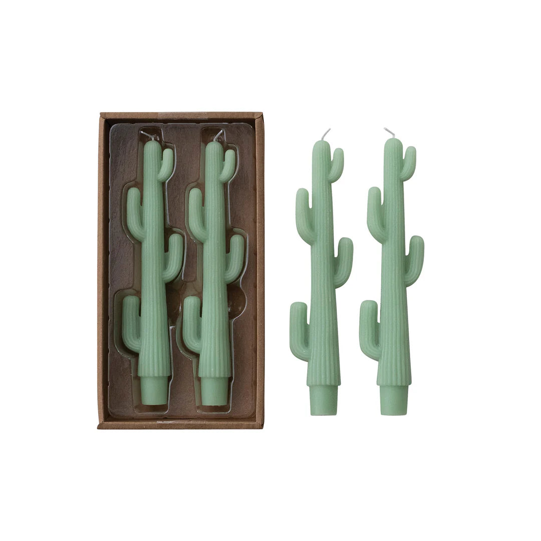 Three sage green cactus-shaped candles, with two displayed standing upright next to their brown cardboard packaging on a white background.