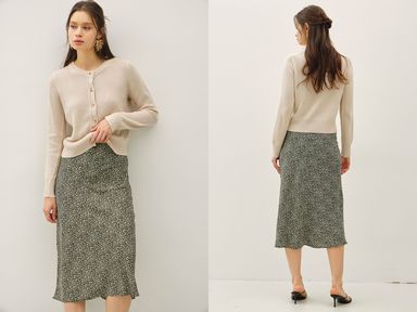 Woman wearing a beige cardigan and patterned skirt, standing against a white background.