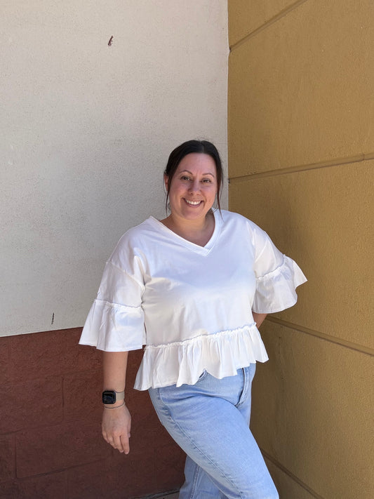 Person wearing a white blouse with ruffled details and light blue jeans on a plain background