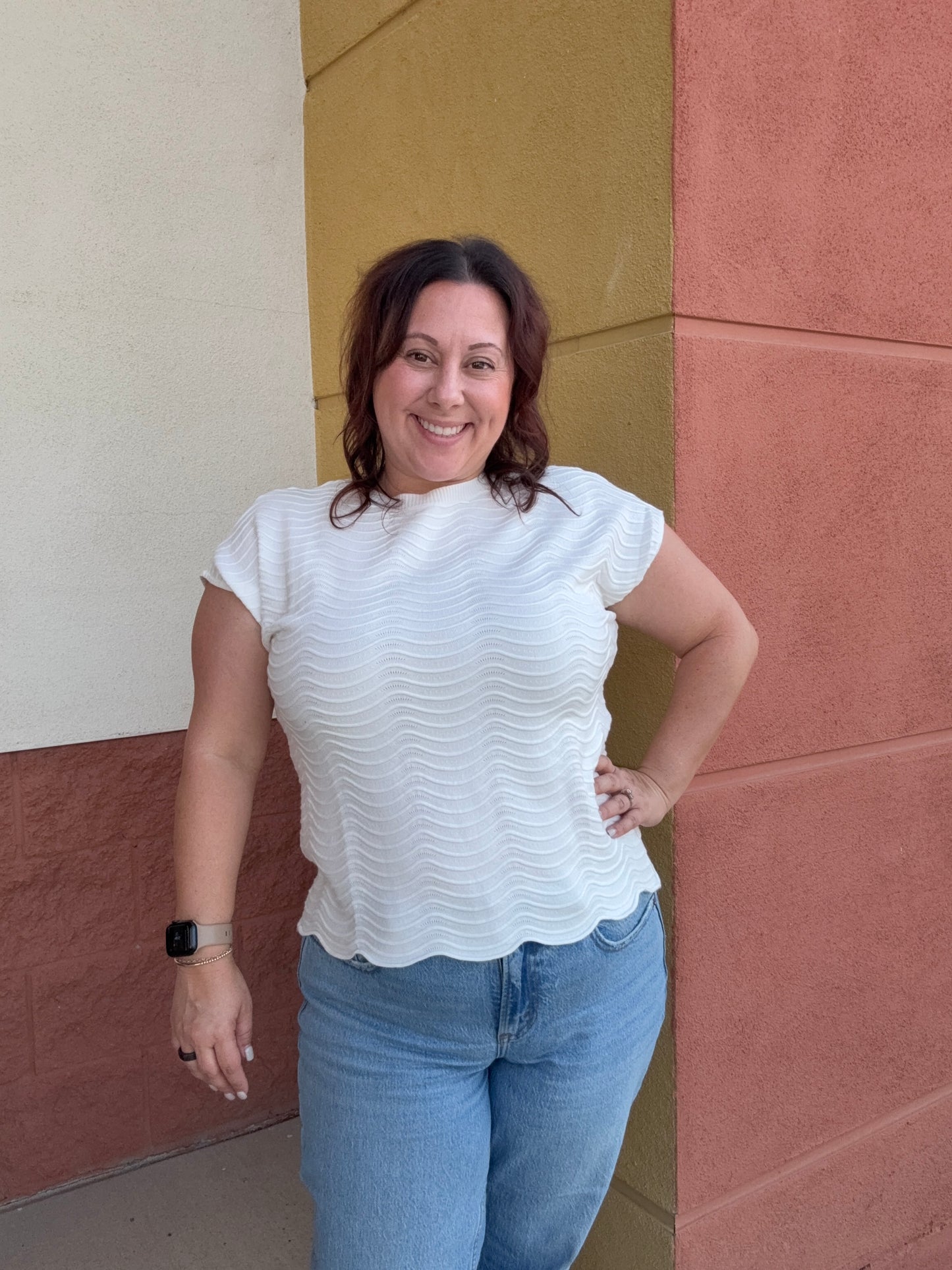 Woman in a white blouse and blue jeans standing on a tiled floor.
