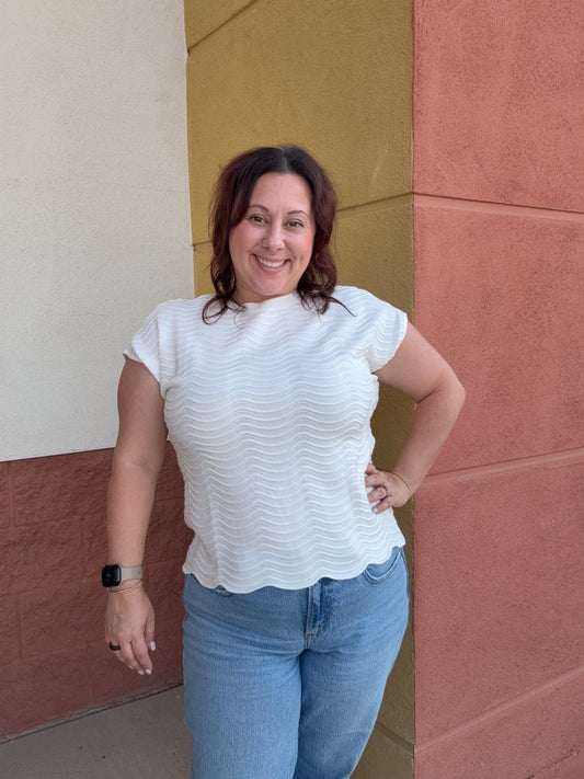 Woman in a white blouse and blue jeans standing on a tiled floor.