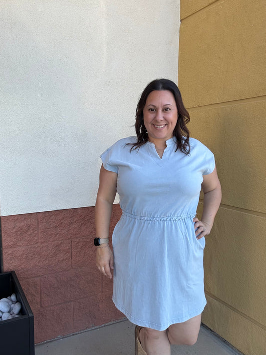 Woman wearing a light blue dress standing against a wall.