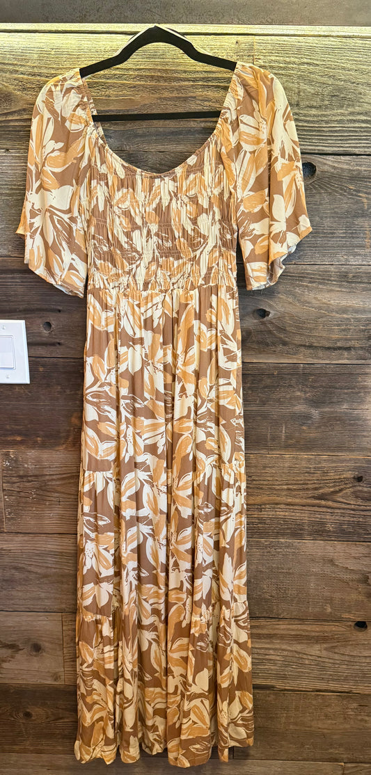 Long dress with a leaf pattern on a hanger against a wooden wall.