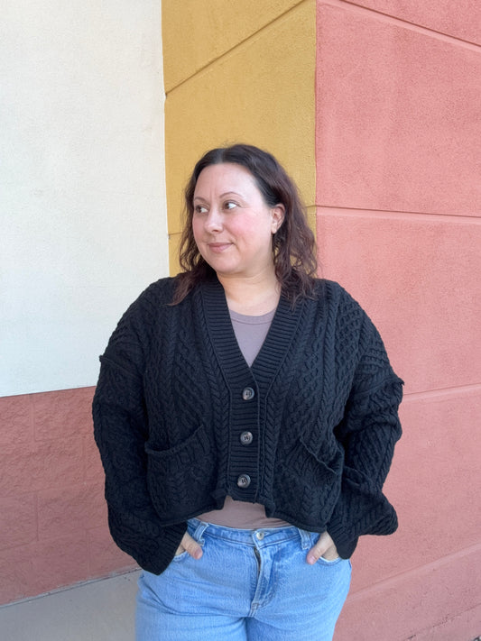 Person wearing a black knitted cardigan and blue jeans standing on a colorful floor.