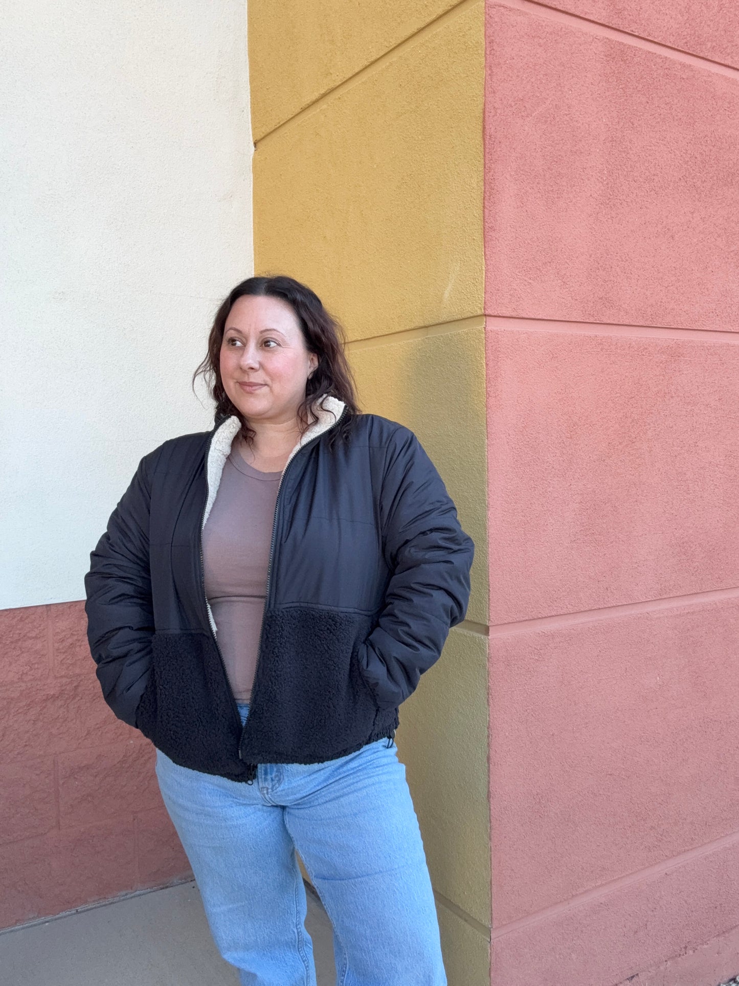 Person wearing a black jacket and light blue jeans standing on a multicolored tiled floor.