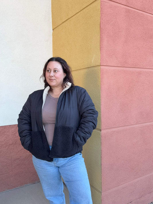 Person wearing a black jacket and light blue jeans standing on a multicolored tiled floor.