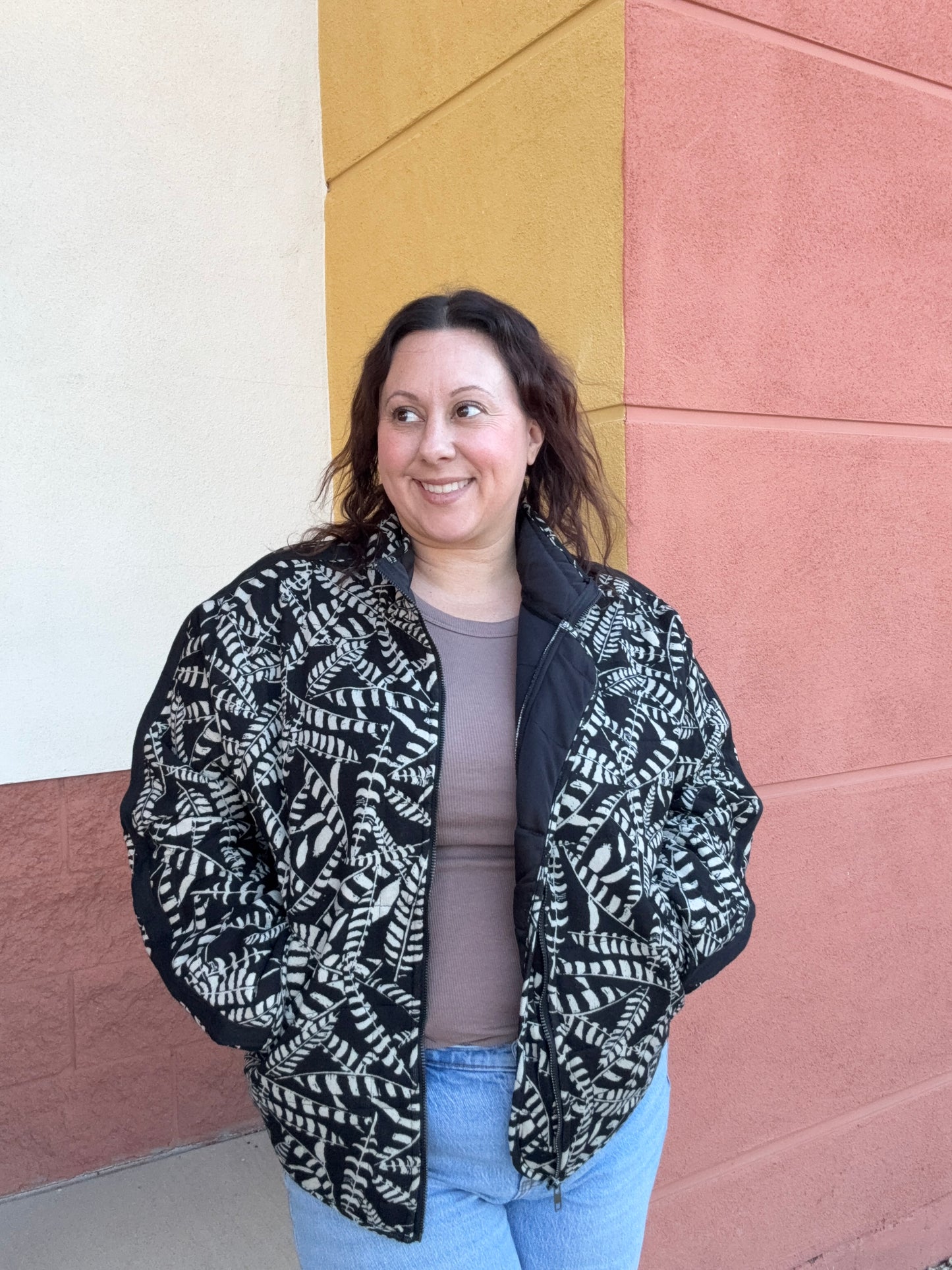 Person wearing a black and white patterned jacket on a colorful floor.