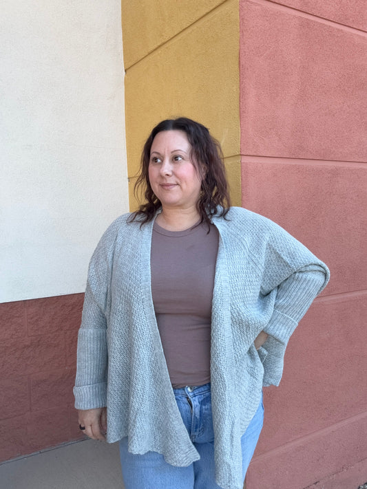 Person wearing a gray cardigan over a brown top on a multicolored floor.