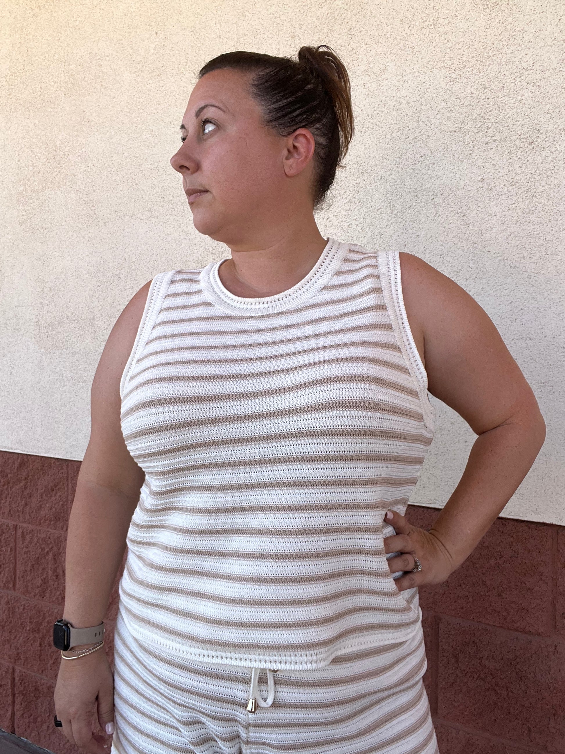 Woman wearing a striped sleeveless top and shorts against a textured wall.