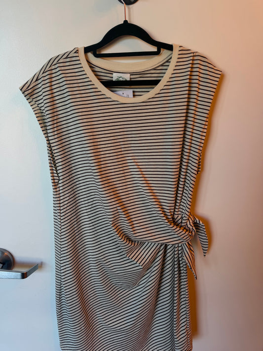 A sleeveless wrap-style dress with thin horizontal black stripes on a beige background, hanging on a black hanger against a plain wall.