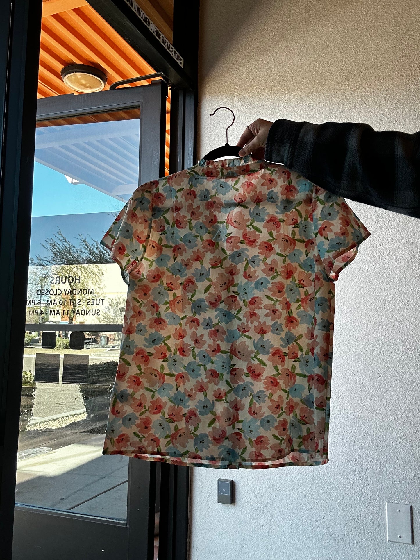 Floral-patterned shirt held by a person against a reflective surface with a building in the background