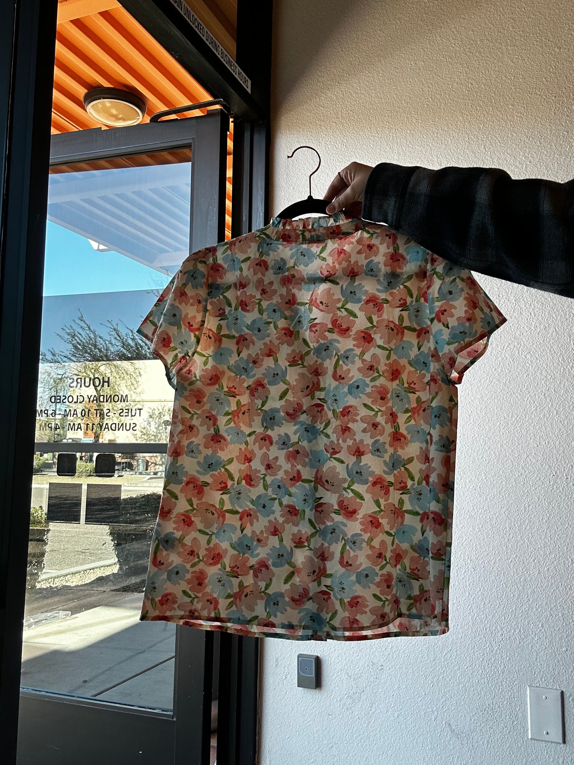 Floral-patterned shirt held by a person against a reflective surface with a building in the background
