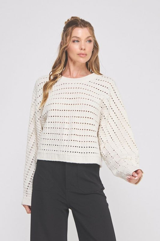 Woman wearing a white textured sweater and black pants on a light gray background