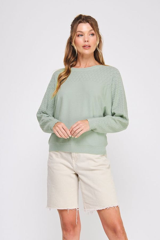 Woman wearing a light green sweater and beige shorts on a white background