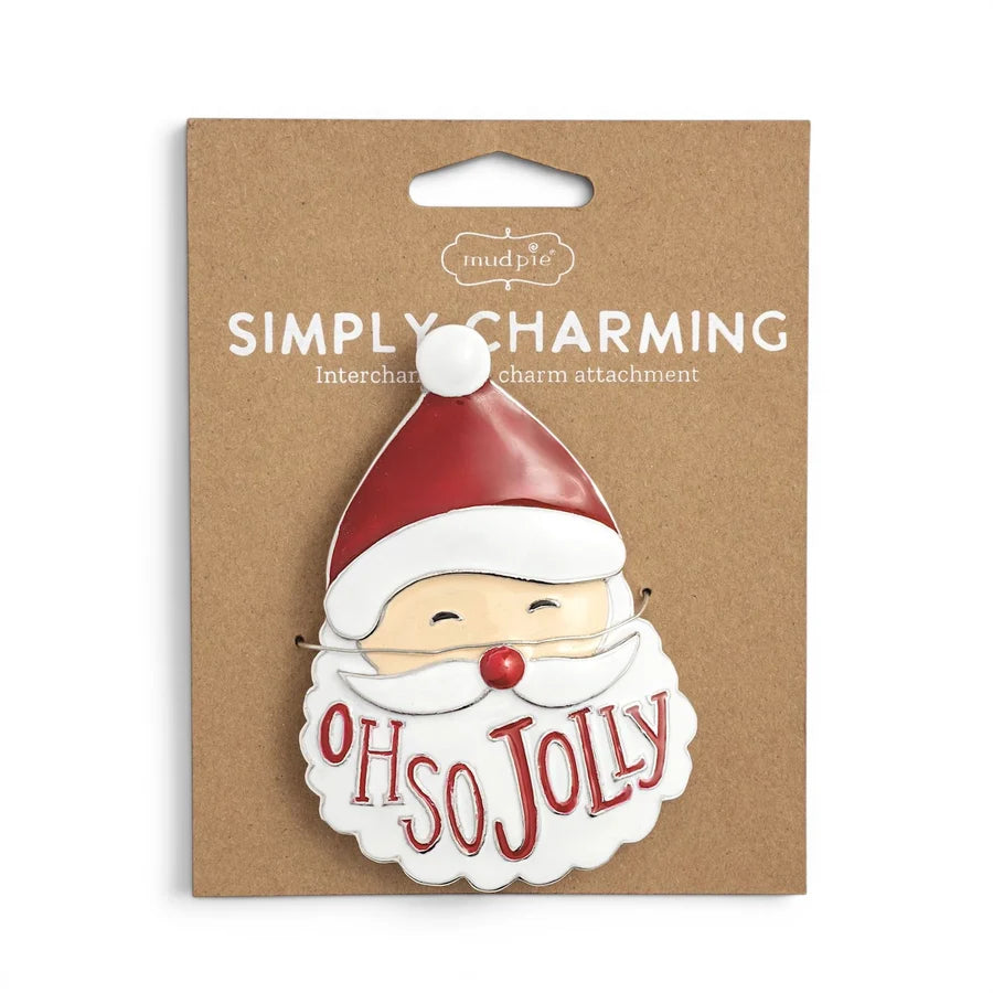 A Santa face enamel charm with the words 'OH SO JOLLY' on a brown kraft backing card labeled 'Simply Charming' by Mudpie.
