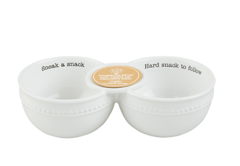 A white ceramic two-bowl snack tray with black printed text reading 'Sneak a snack' on the left bowl and 'Hard snack to follow' on the right bowl, connected by a small round gold center piece, on a white background.